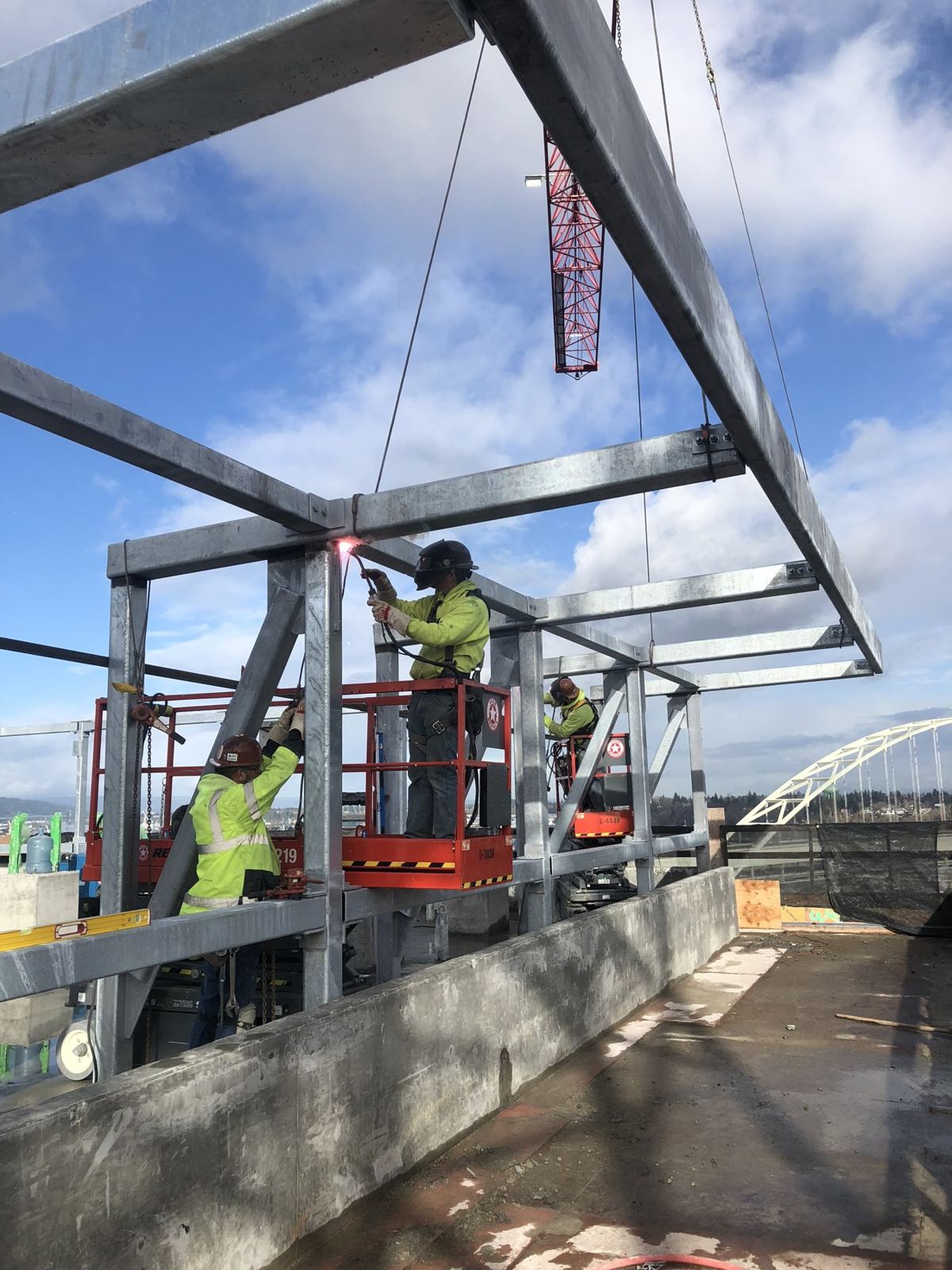 Ironworkers bolting rooftop canopy steel from a lift